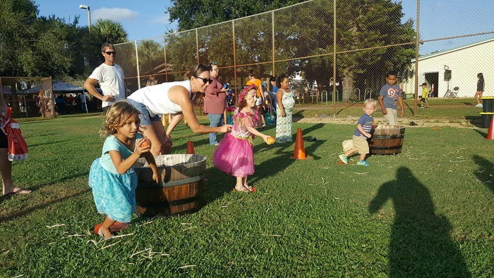 Kids playing an apple relay game on the grass at a South Florida fall festival