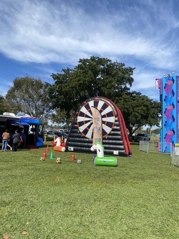 Giant inflatable dart game next to an inflatable slide at a park event in Palm Beach County