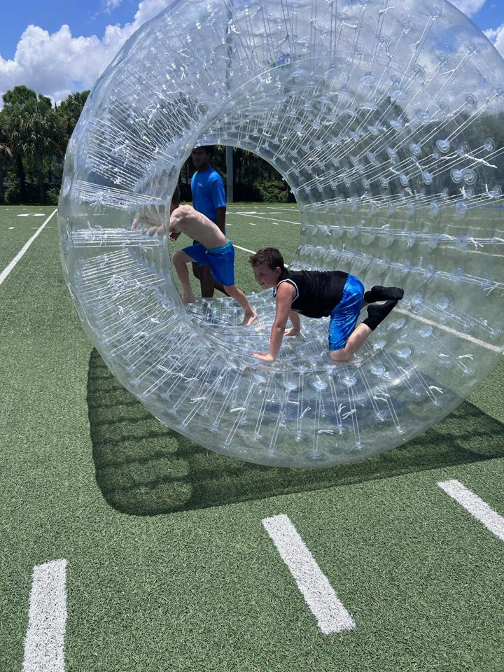 Kid rolling in a clear hamster wheel on a school field