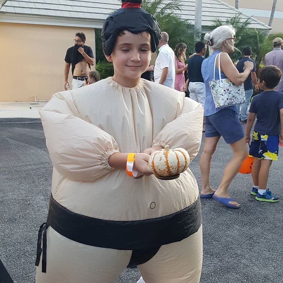 Boy in an inflatable sumo costume holding a small pumpkin at a Crazy Games fall festival in Palm Beach County