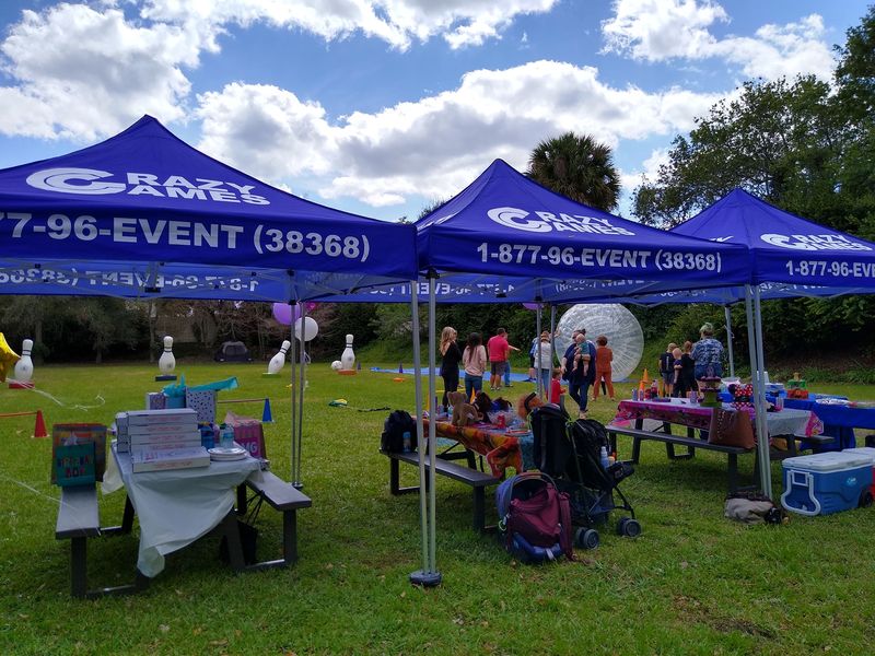 Crazy Games FL branded shade tents over game stations at an outdoor party in a Palm Beach County park