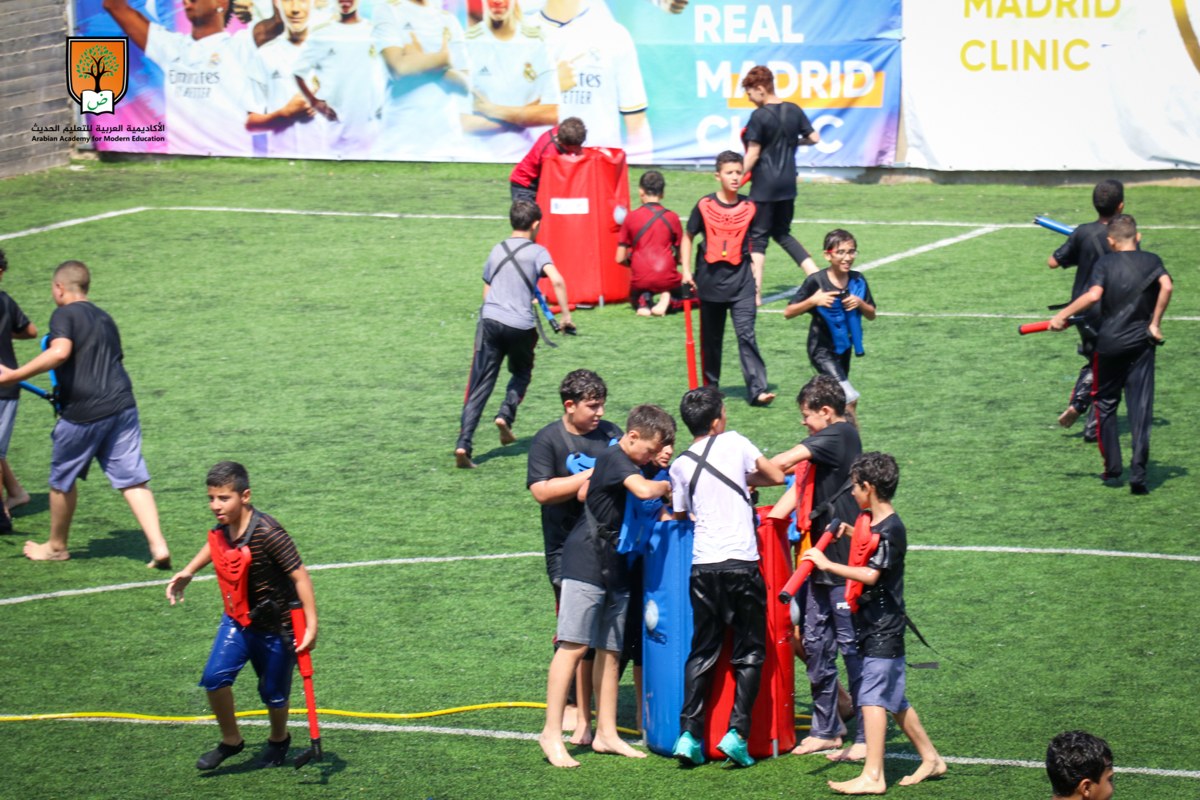 Two teams of kids playing Crazy Water Tag with vests and water guns on a grass field