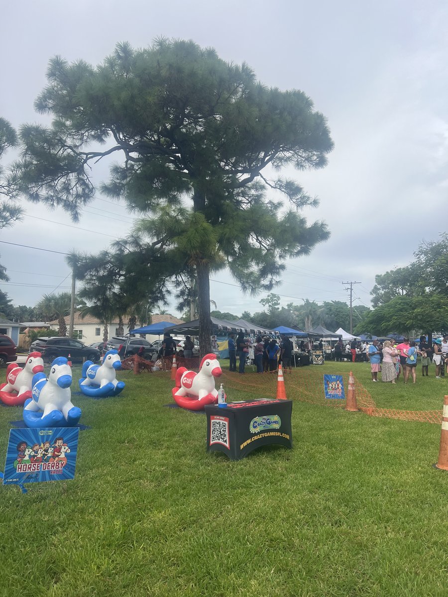 Crazy Games FL derby horse race game set up on the grass at an outdoor community festival with vendor tents