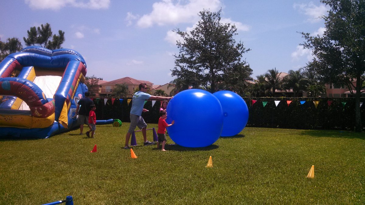 Kids pushing giant blue push balls across a backyard lawn at a party