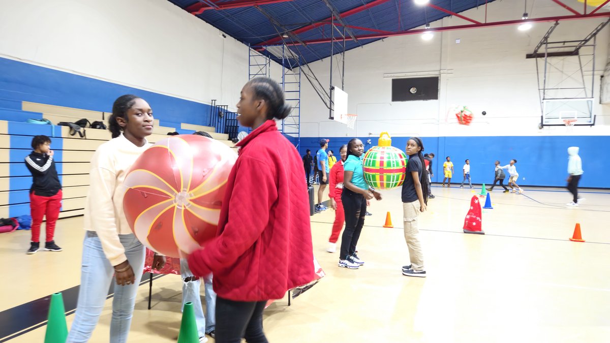 Teens carrying a giant ornament in the Crazy Games FL Giant Ornament and Spoon Race at an indoor school gym holiday party