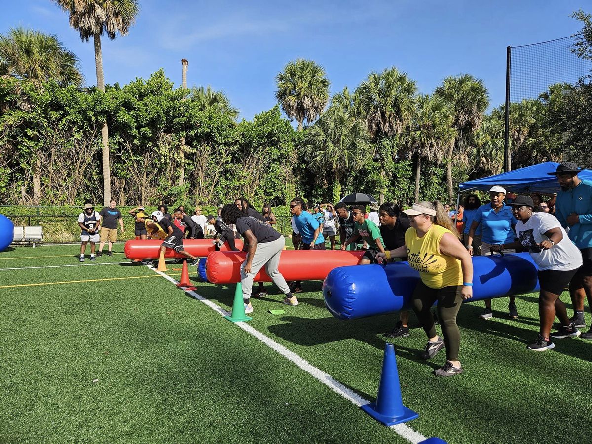 Adult teams lined up on giant inflatable pens during a relay race on a turf field
