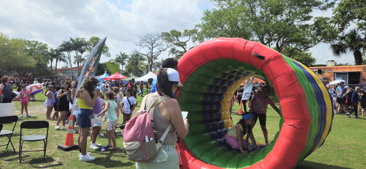 A Crazy Games FL inflatable hamster wheel rolling on the lawn at a busy community festival in Palm Beach County