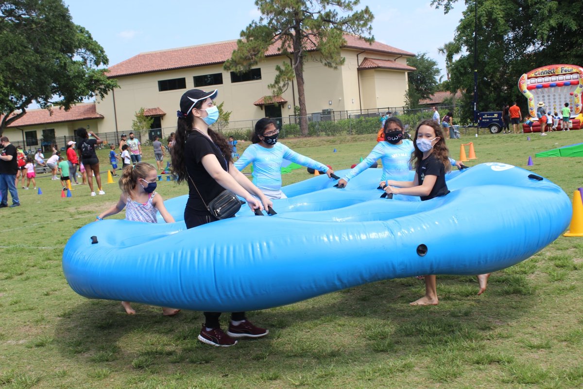Kids and adults carrying a giant blue inflatable honeycomb in a team relay race on a school field