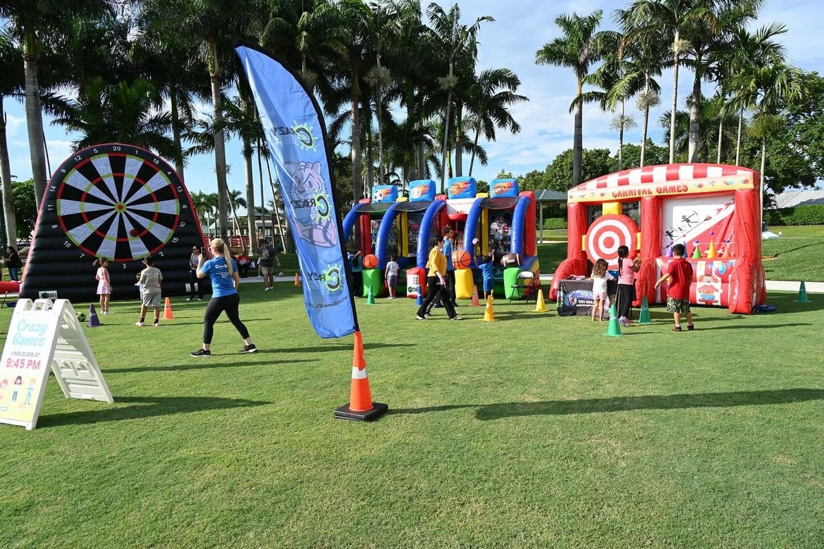 Crazy Games FL inflatable carnival game, sports challenge and giant soccer dartboard set up on a park festival lawn with palm trees