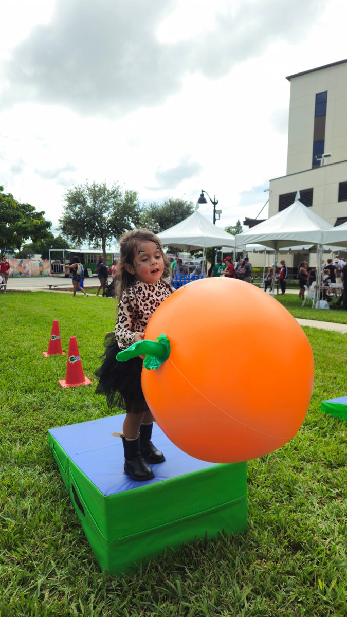 Little girl pushing a giant inflatable pumpkin ball at a Crazy Games fall festival game zone