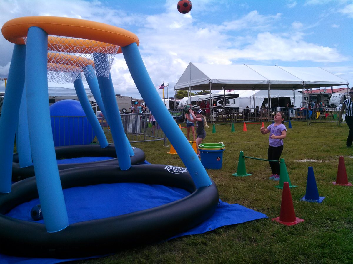 Kids shooting at the Crazy Games Jumbo Basketball inflatable hoop at an outdoor school festival with tents in Palm Beach County