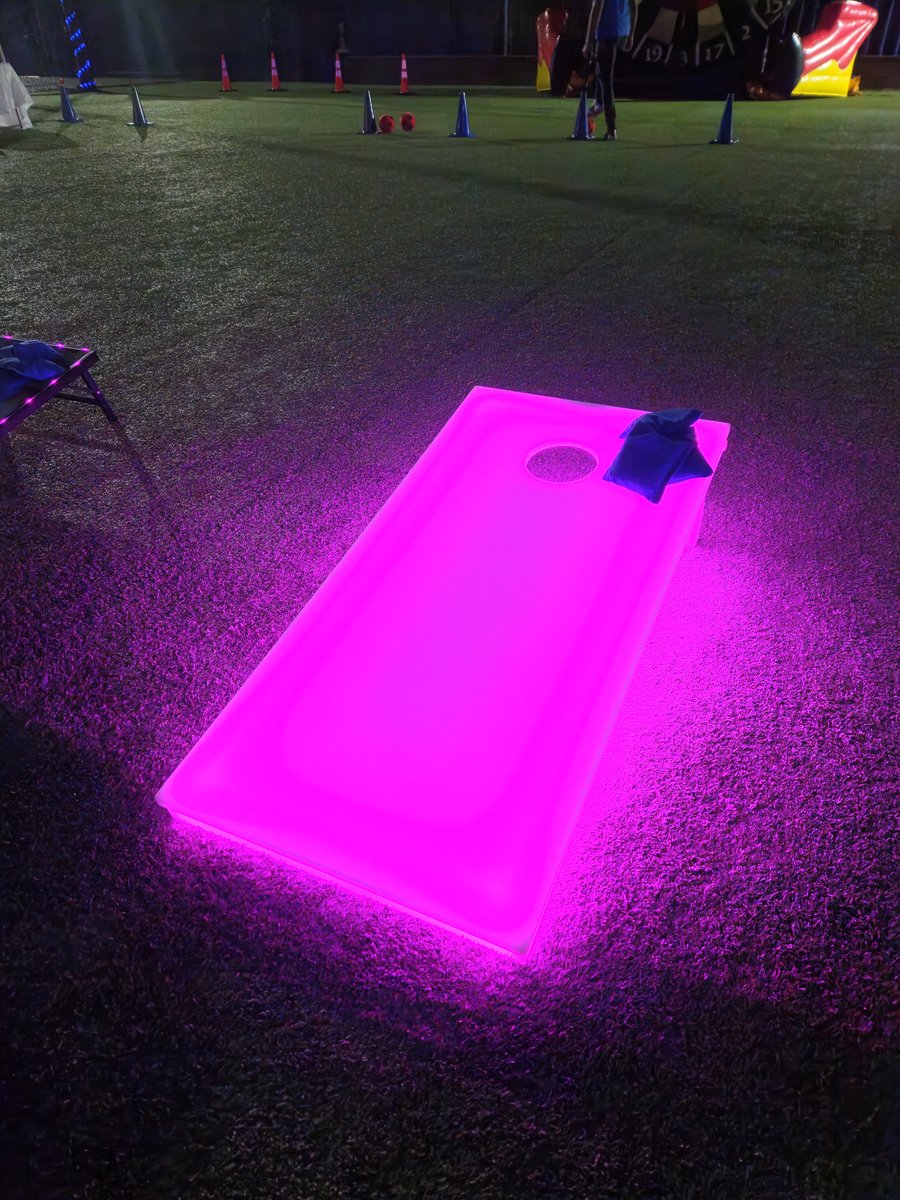 Pink glowing LED lighted cornhole board on the lawn at a night party in Palm Beach County