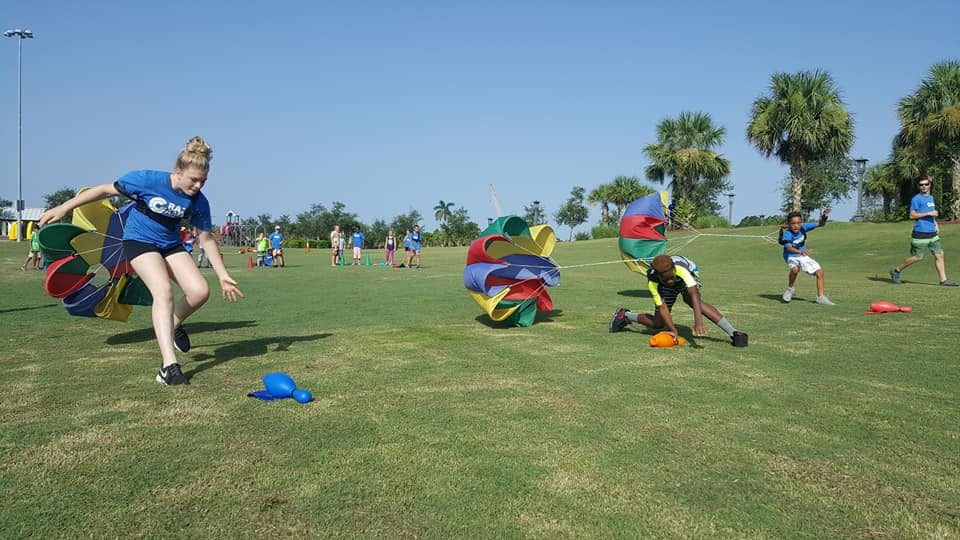 Kids and a Crazy Games FL coach racing with colorful drag parachutes across a park field in South Florida
