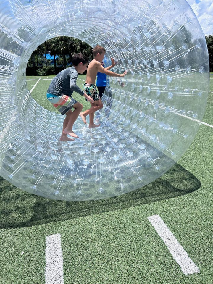 Kids rolling inside a clear hamster wheel on a school field