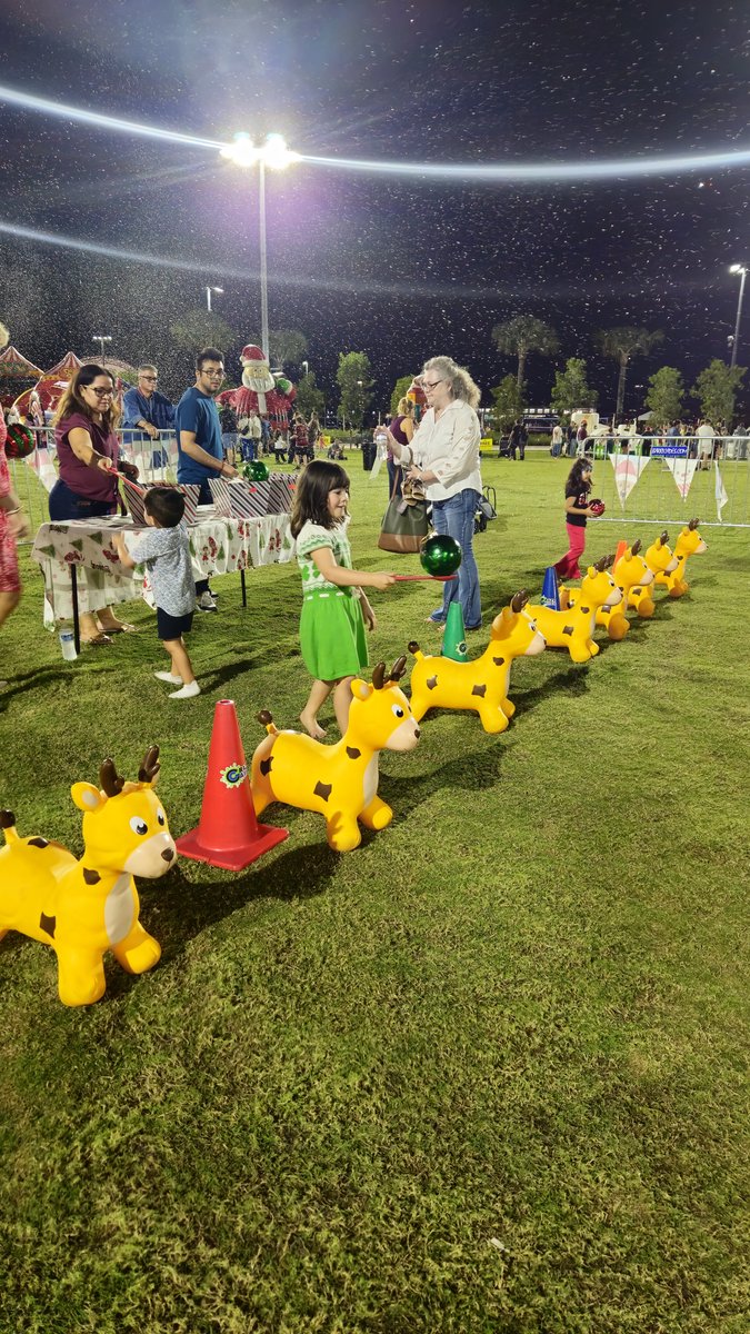 Kids lined up on inflatable hoppers for a Reindeer Hop Race on a lit field at night while families watch