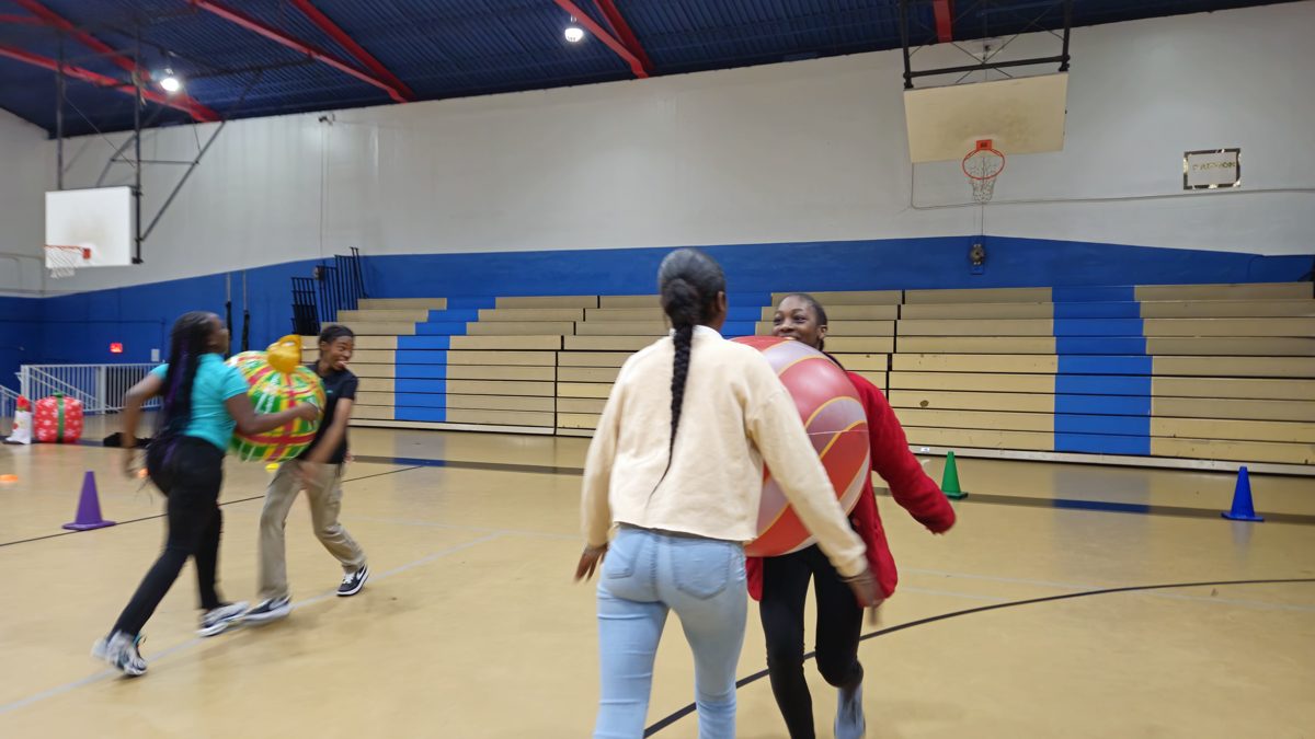 Students running across a school gym carrying giant Christmas ornaments during a holiday relay race