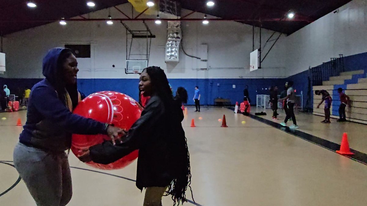 Teens passing a giant red Christmas ornament during a Crazy Games FL holiday relay in a school gym