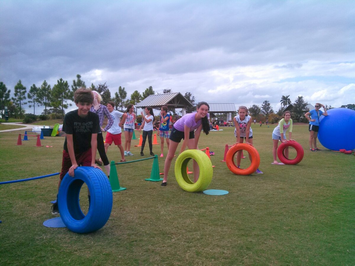 Wide view of tire race field games set up on a grass field near trees and a pavilion in South Florida