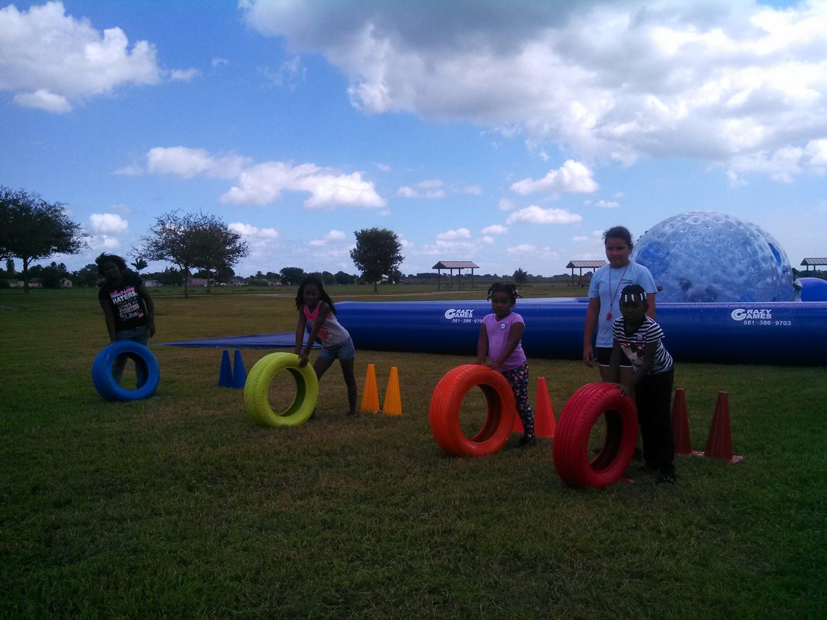 Kids racing colorful tires on a field at a Crazy Games community event in Palm Beach County